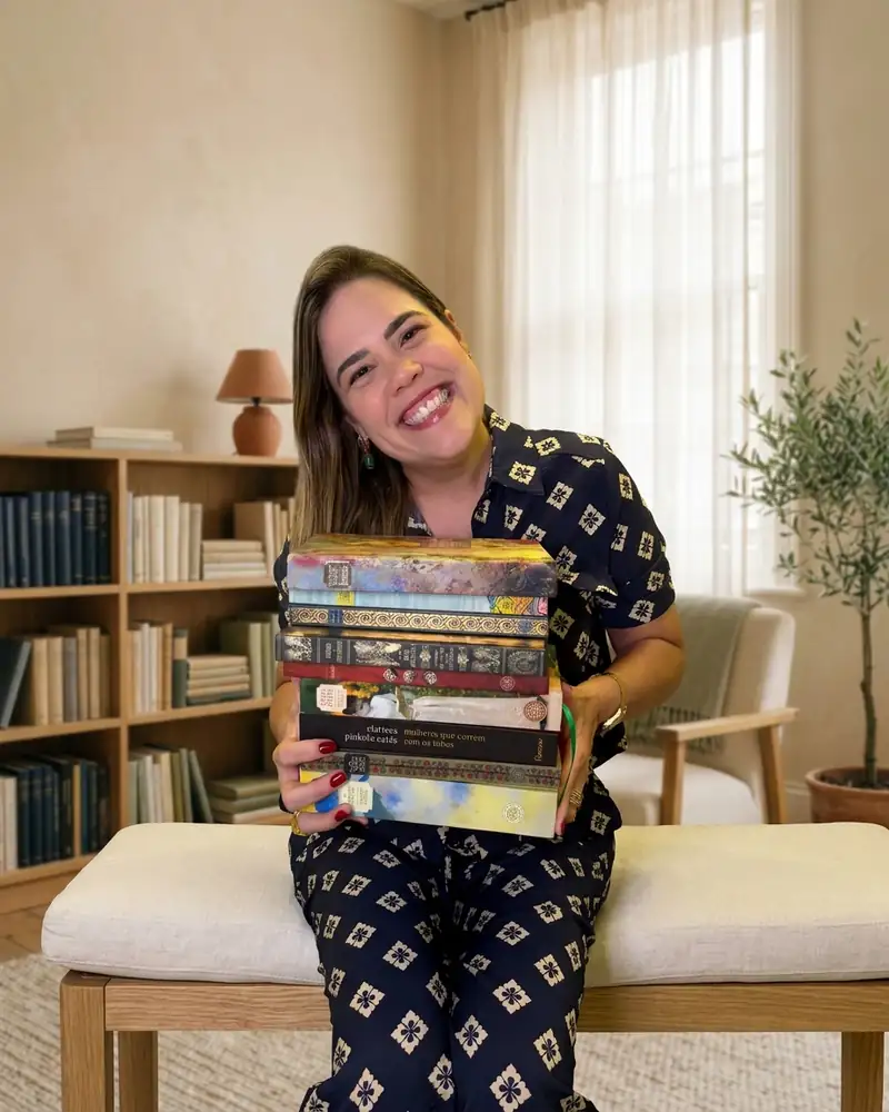 Daniella Xavier sentada, abraçando uma pilha de livros e sorrindo