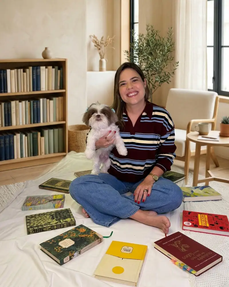 Daniella Xavier sentada com seu cachorro no colo, entre livros