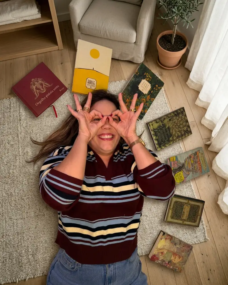 Daniella Xavier rindo e fazendo óculos com as mãos, entre livros
