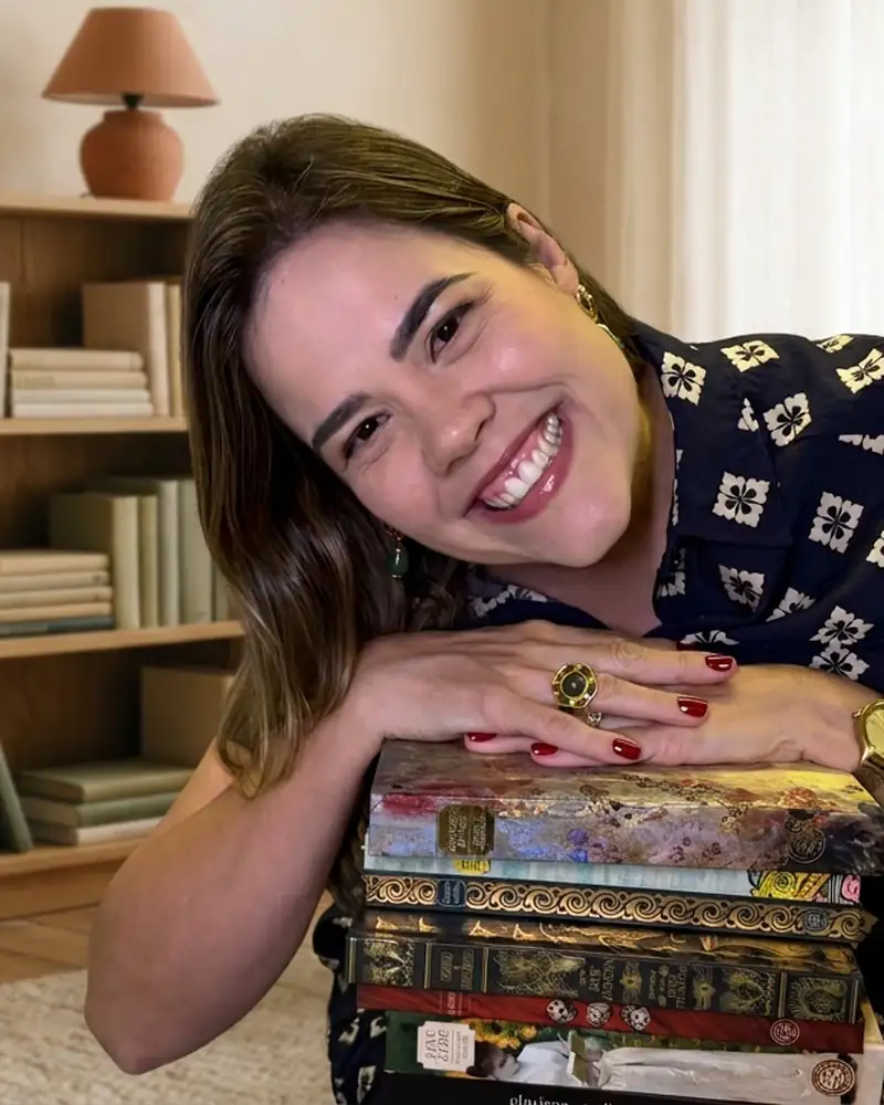 Daniella Xavier sorrindo, com a cabeça apoiada numa pilha de livros